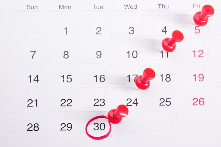 Close-up of a calendar with red push pins marking important dates, emphasizing deadlines.