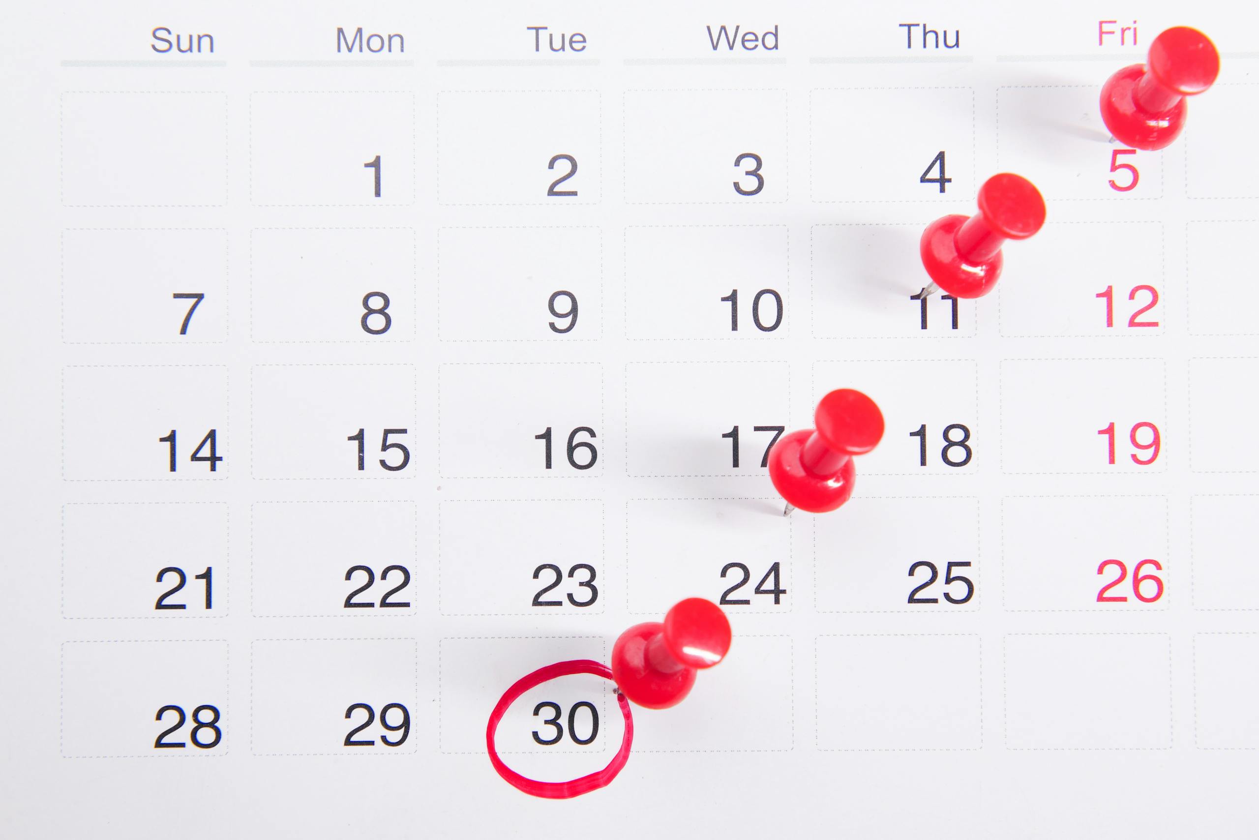 Close-up of a calendar with red push pins marking important dates, emphasizing deadlines.