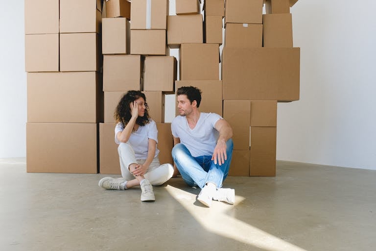 Woman touching cheek and talking to boyfriend with crossed legs while looking at each other on floor with cardboard containers during relocation