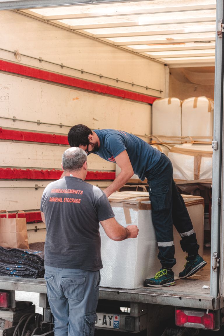 Faceless removal porters in uniform unloading big white boxes off lorry while working in delivery service